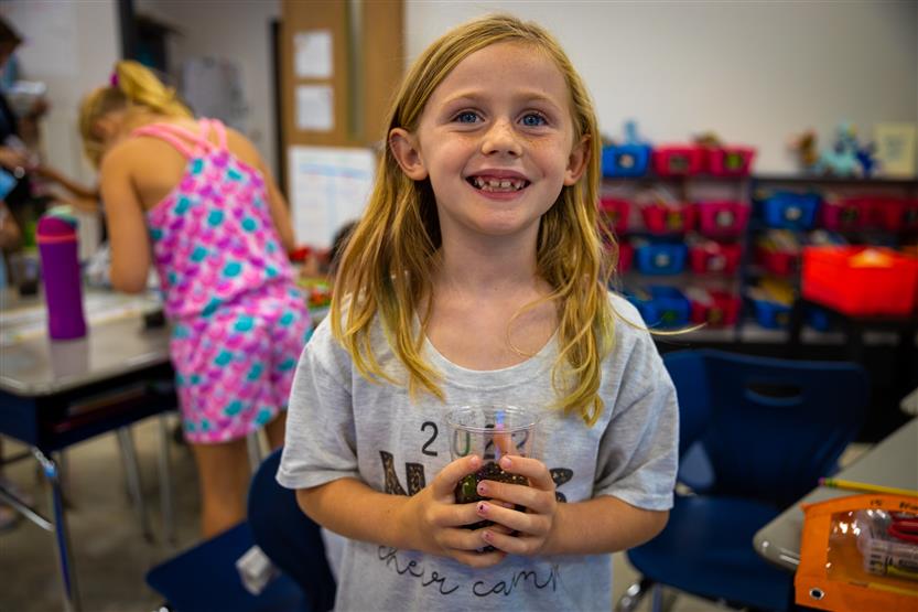A blonde girl smiles while holding a seed in a cup